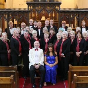 Castell Coch Choral Society. A mixed choir dressed in formal black with red flashes. Conductor and Accompanist sit in front.