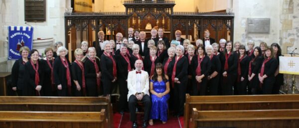 Castell Coch Choral Society. A mixed choir dressed in formal black with red flashes. Conductor and Accompanist sit in front.