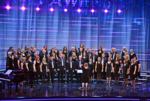 Cor Caerdydd. Large mixed choir all wearning black in formation on the Eisteddfod stage