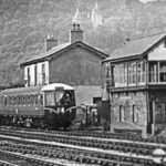 Train through Radyr. Passing the signal box in a black and white photo